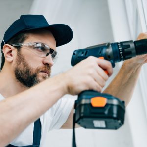 adult-repairman-in-goggles-fixing-window-handle-by-electric-drill.jpg